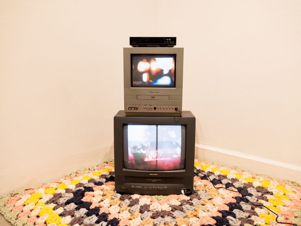 Two TV stacked on a handmade rug on the floor. The TVs are playing two different films.