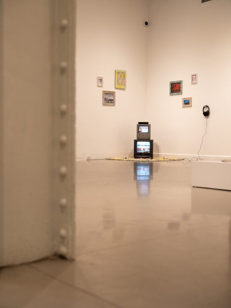 An art installation with two televisions stacked sits in the corner of a gallery.